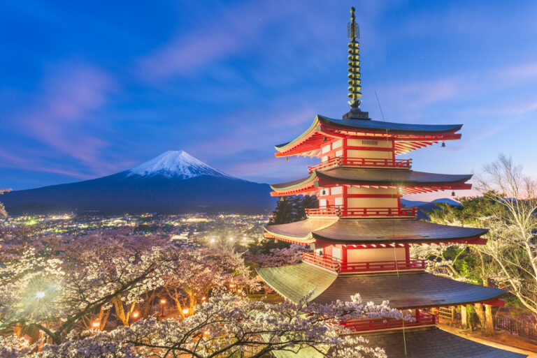 Fujiyoshida, Japan view of Mt. Fuji and pagoda in spring season with cherry blossoms at dusk.