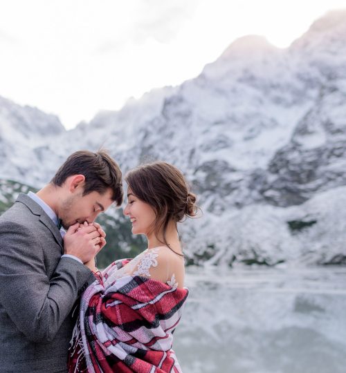 Freezing wedding couple is warming up together in the winter mountains in front of frozen lake
