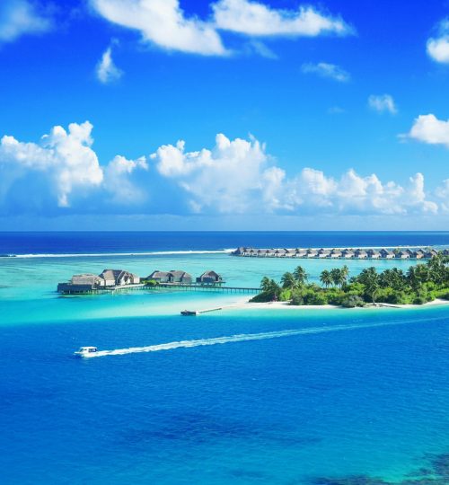 Crystal clear waters surround a luxurious Maldives resort under a bright blue sky.